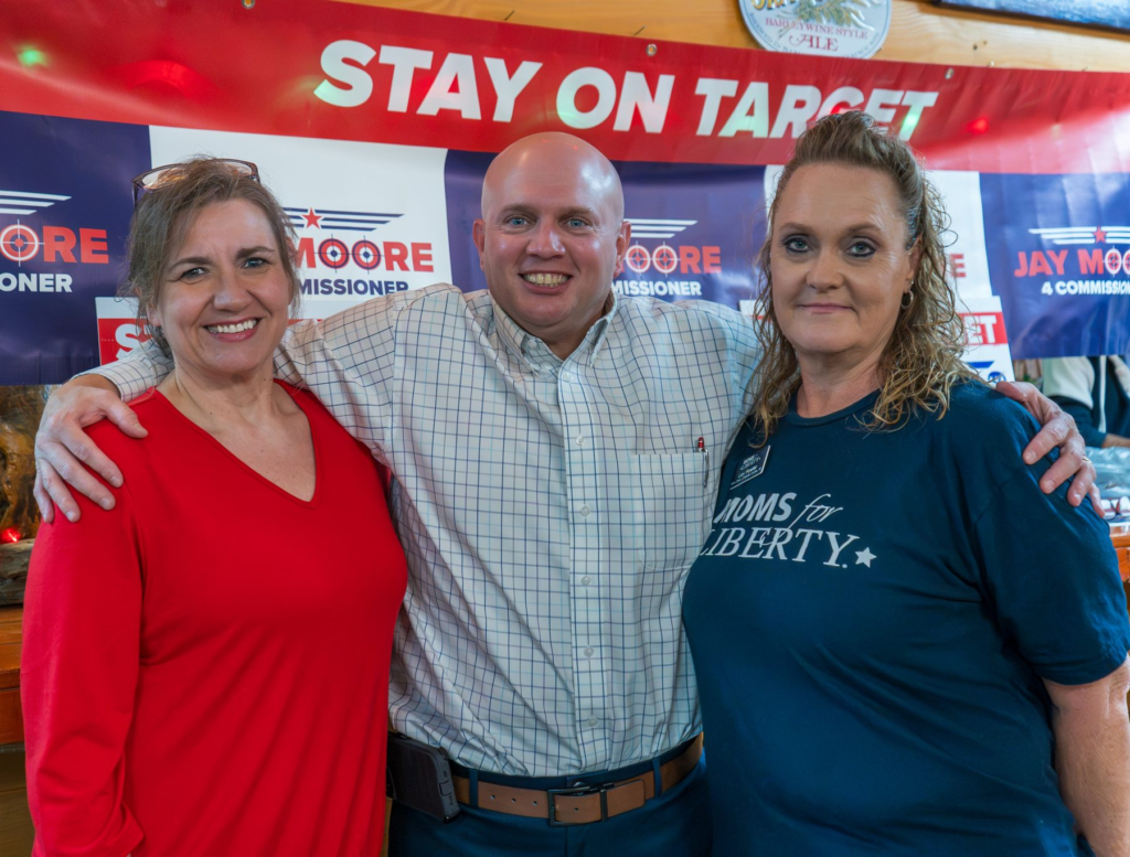 Jay Moore, bald in a light windowpane-check shirt, smiling with two neighbors in front of Stay on Target banners