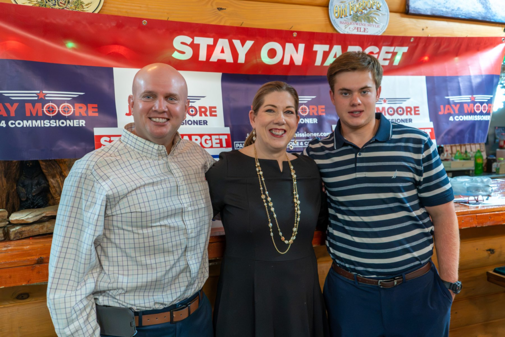 Jay Moore, bald in a light windowpane-check shirt, with two neighbors at a campaign event